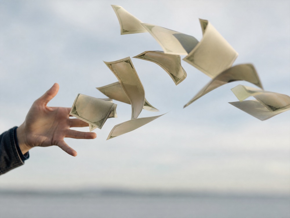 An open hand releasing cash into a gust of wind