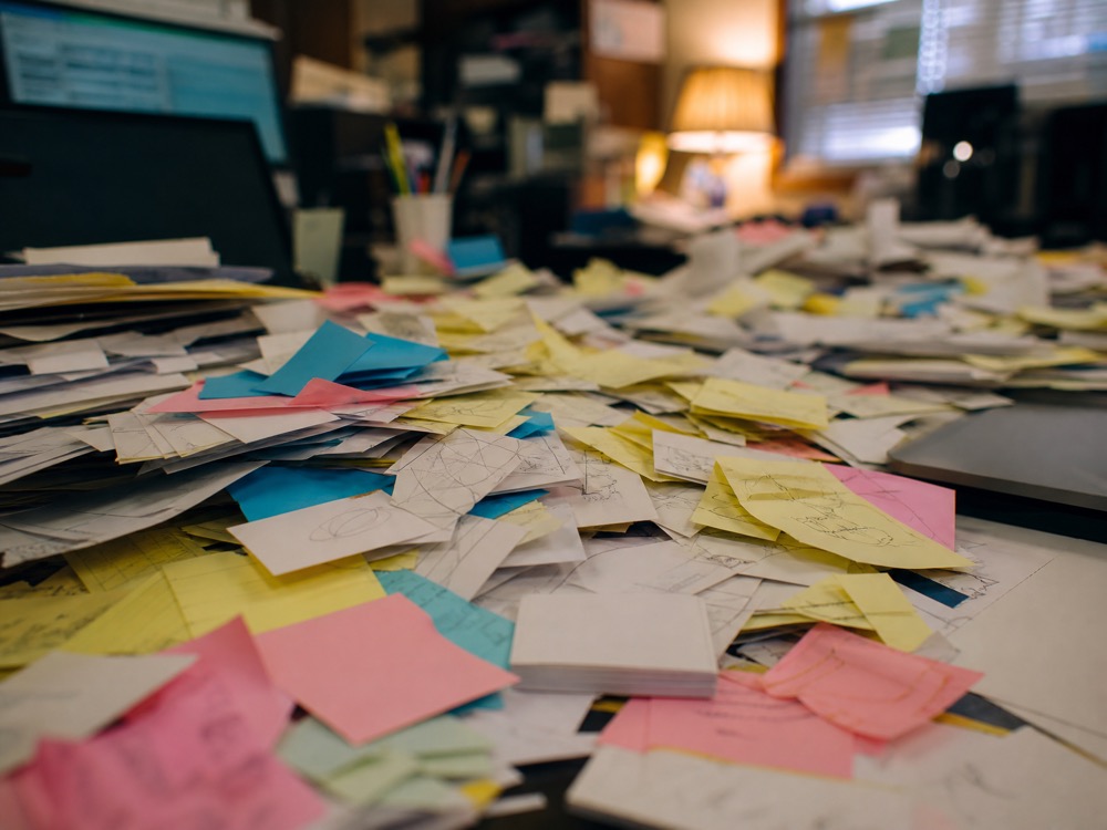 A desk buried in scattered sticky notes and business cards
