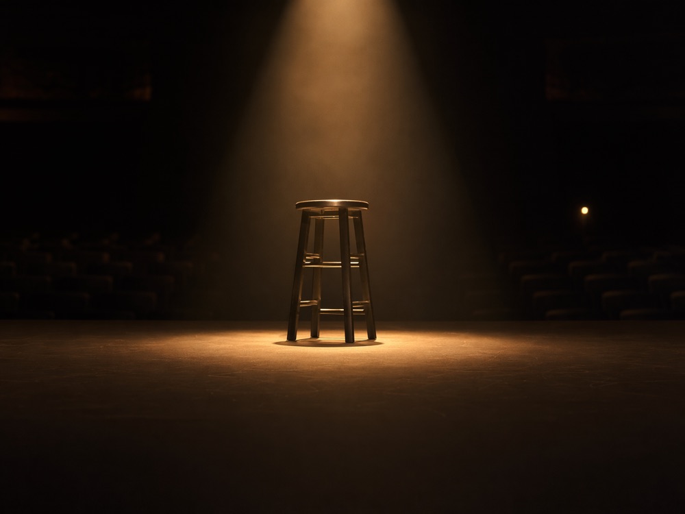 A single empty stool under a spotlight, an audience waiting